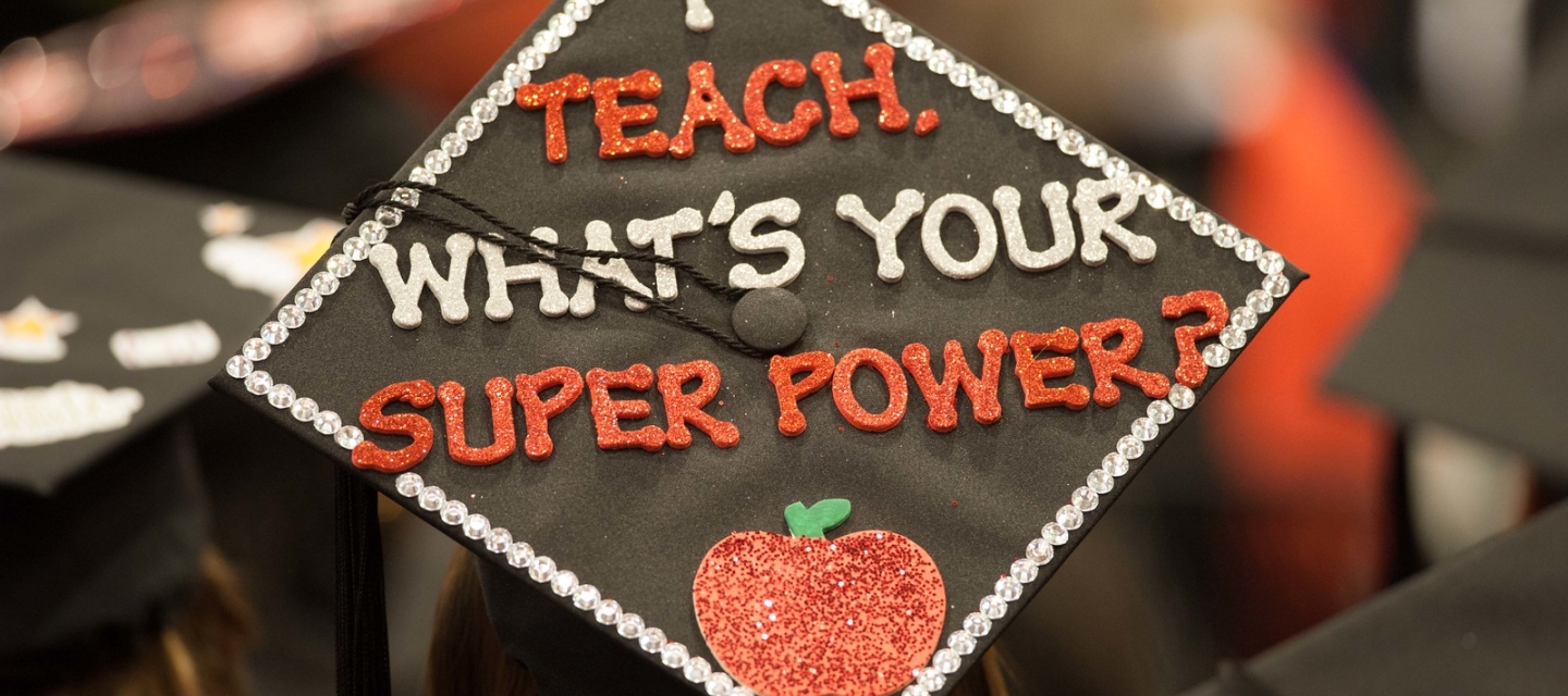 Student at Commencement with "I teach, what's your super power?" on mortarboard cap